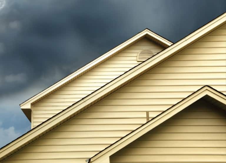 Casa con revestimiento amarillo y nubes de tormenta asomándose por detrás