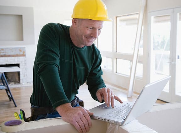 Contratista usando un casco protector color amarillo mientras mira su computadora portátil en el lugar del trabajo